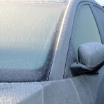 Driver clearing ice from a frozen car windscreen using a plastic scraper