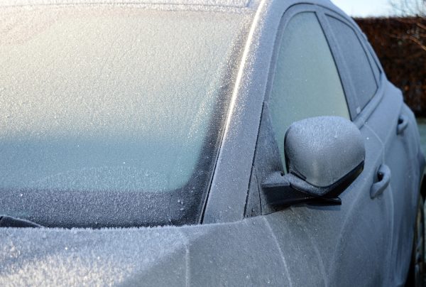 Driver clearing ice from a frozen car windscreen using a plastic scraper